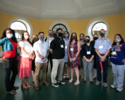 A group of masked people standing together in a room with round windows.