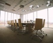 An empty board room with a large oval table and rolling chairs.
